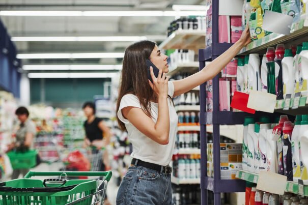 Using smartphone. Female shopper in casual clothes in market looking for products.